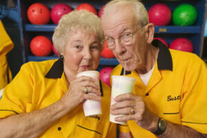 Older couple in bowling shirts sharing drinks at a bowling alley